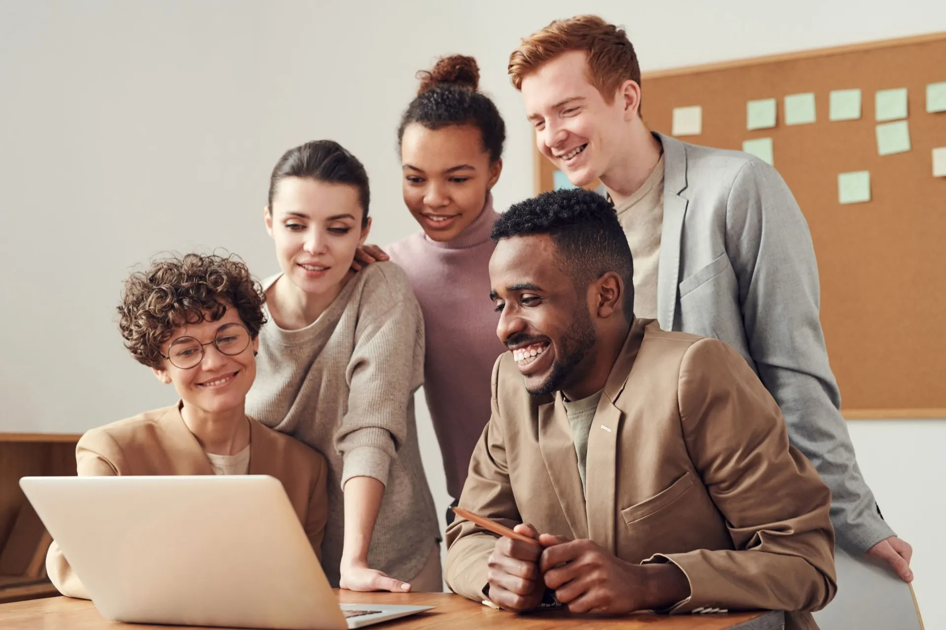 Cinq personnes sourient en regardant ensemble l'écran d'un ordinateur portable